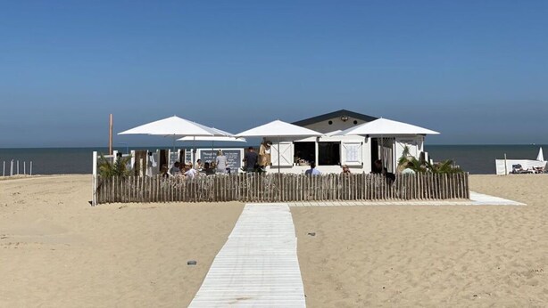 A beachside building with white umbrellas and a wooden fence. - Schmitz 2 Comfortable Holiday Residence (De Haan)