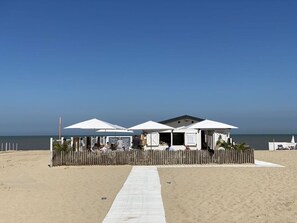 Un bâtiment situé au bord de la plage, avec des parasols blancs et une clôture en bois.