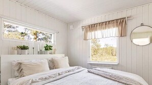 A bedroom with a bed, a window with a view of trees, a mirror, and a bedside table with a lamp. - 6 Person Holiday Home in Mariefred-by Traum (Mariefred)