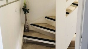 Un escalier avec une finition en bois clair, des murs blancs et une petite plante en pot placée à gauche.