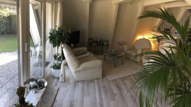 Un salon moderne avec un canapé, une table basse et un téléviseur. Il y a une grande fenêtre et une plante dans le coin.