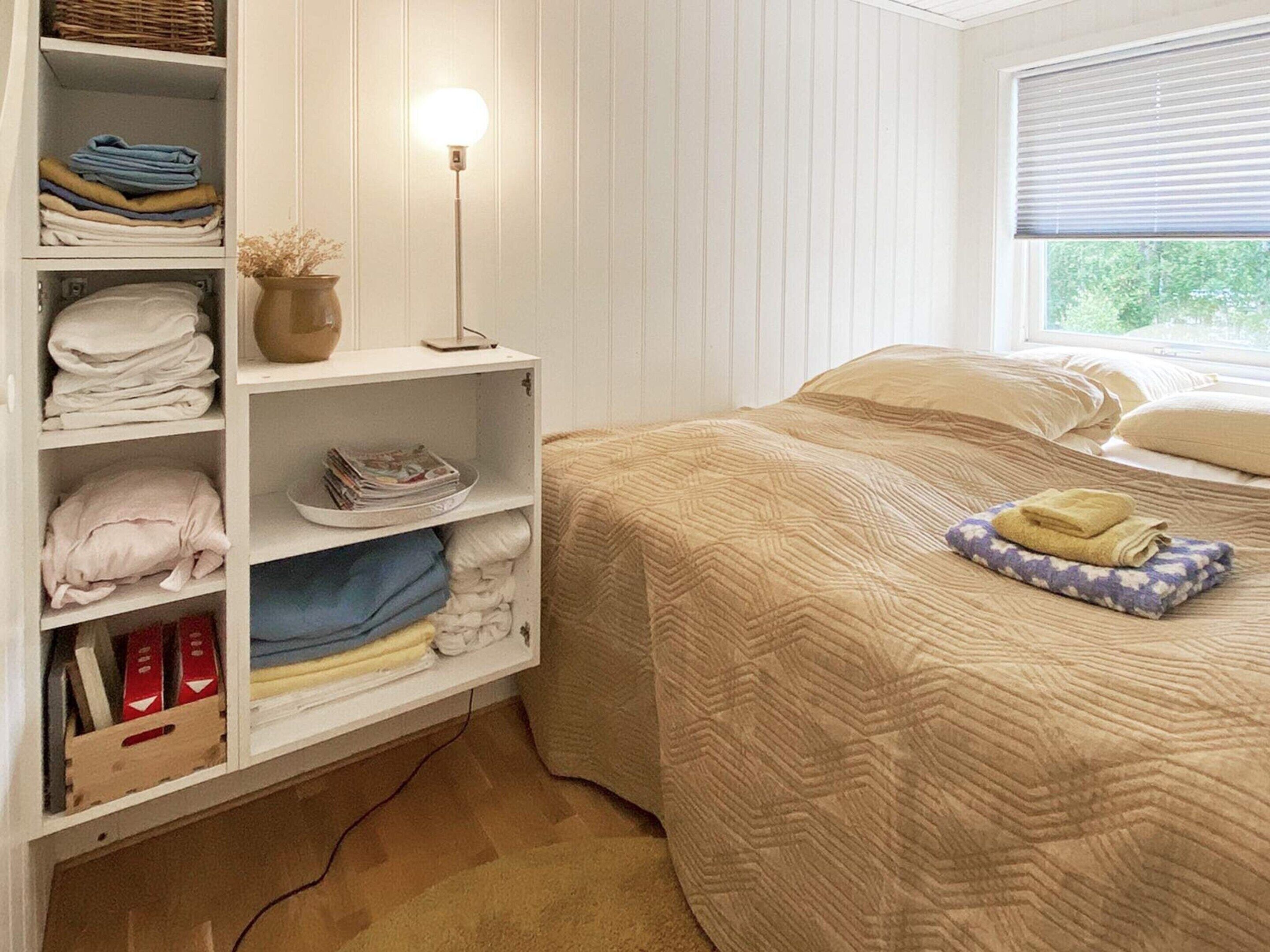 Siisti ja järjestelmällinen makuuhuone, jossa on sänky, yöpöytä lampun kanssa ja ikkuna, jossa on sälekaihtimet.