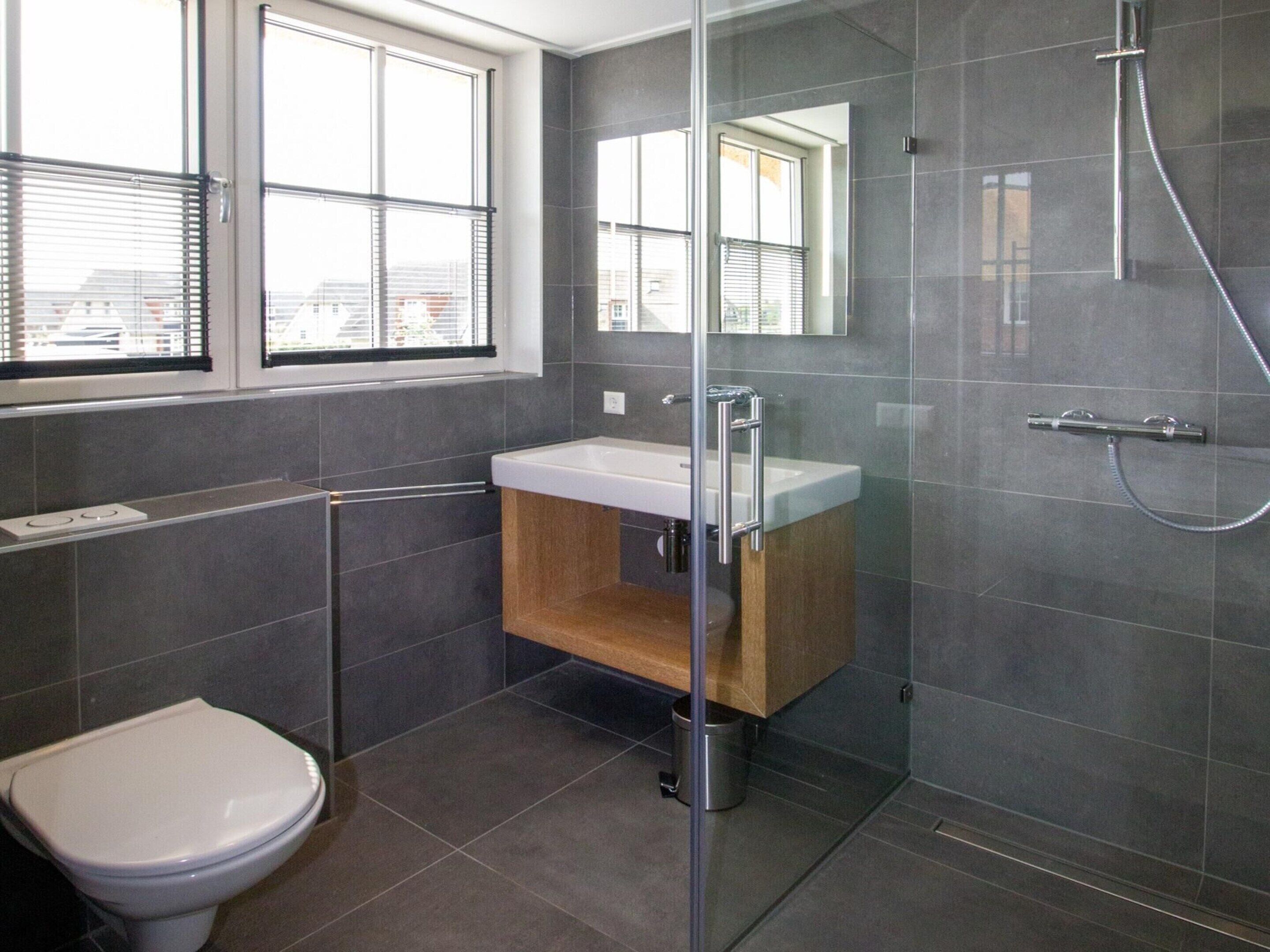 A modern bathroom with a glass shower enclosure, a white sink, and a toilet.