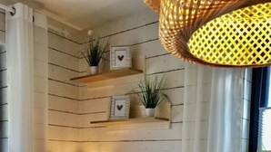 Ein gemütliches Wohnzimmer mit einem schwarzen Sofa, einem kleinen Beistelltisch mit Lampe, Zimmerpflanzen und einer gewebten Leuchte.