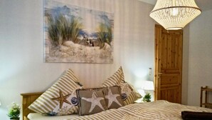 Ein Schlafzimmer mit einem Bett, gestreifter Bettwäsche, Sterntangenkissen, einem Gemälde mit Strandmotiv und einer Holztür.