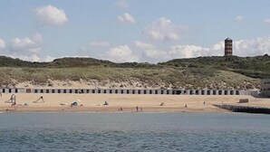 Une plage bordée de cabanes de plage, avec un phare en arrière-plan.