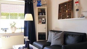 A living room with a black leather sofa, a white coffee table, a blue lamp, and a bookshelf with framed photos. - Overt Meer 6 Modern Retreat (Grosefehn)