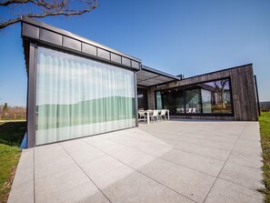 A modern house with a large sliding glass door, a patio with outdoor furniture, and a view of the countryside. - Holiday Home in Somme Leuze for 7 Person (Somme-Leuze)