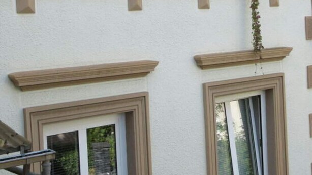 A building with multiple windows, each with a white frame and a small balcony with potted plants. - Voor 8 tot 12 Personen (Neumagen-Dhron)