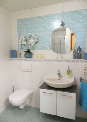 Une salle de bain avec des toilettes, un lavabo et un miroir. Une serviette bleue est accrochée au mur.