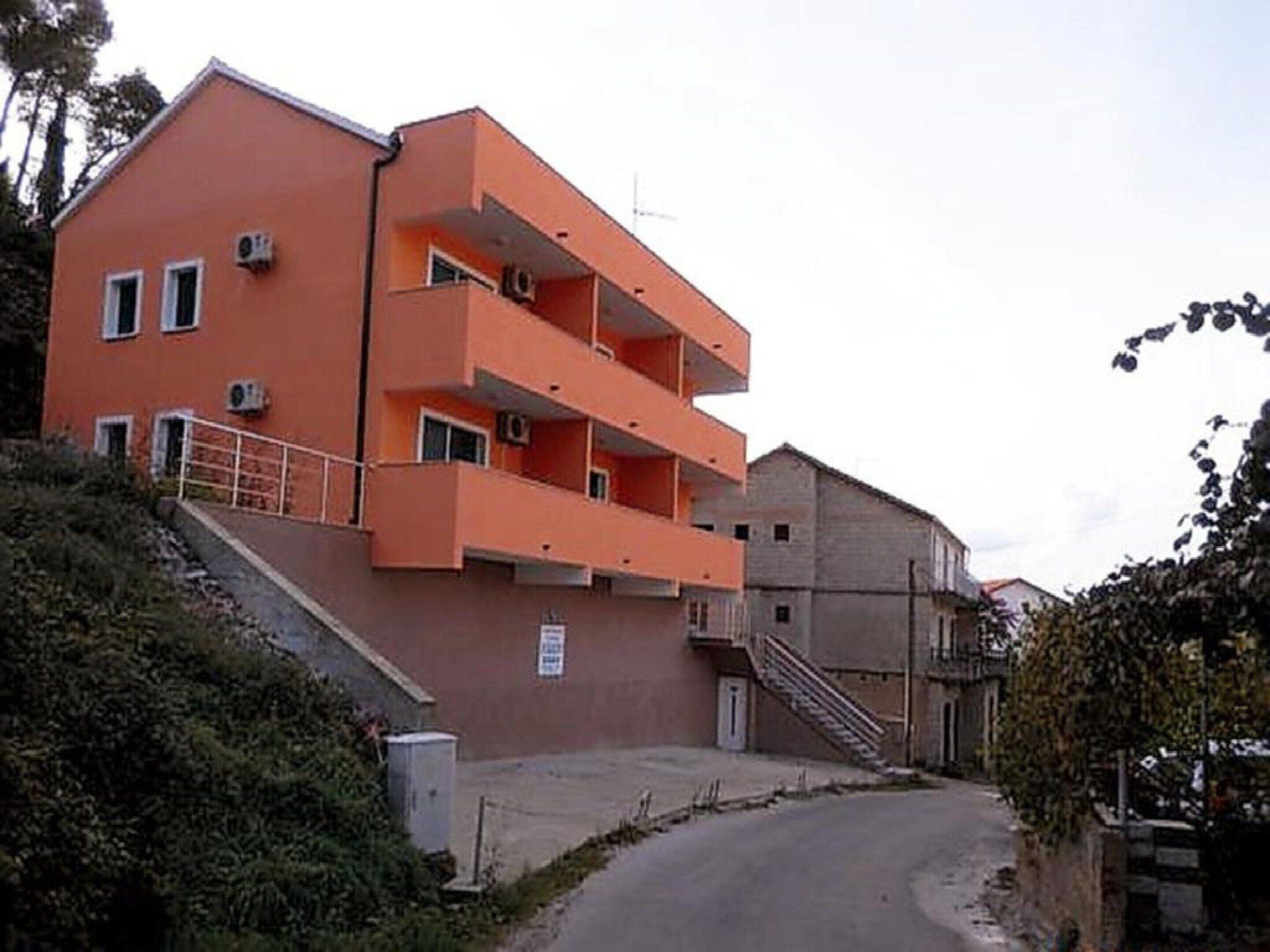 A multi-story building with a red facade, balconies, and a staircase leading to the entrance.