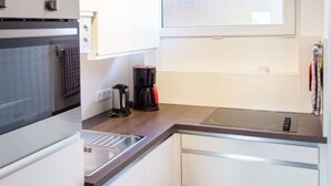 A modern kitchen with white cabinets, a built-in oven, a coffee maker, and a window above the sink.