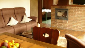 A living room with a brown sofa, a wooden table with fruit, a brick fireplace, and a television on a stand.