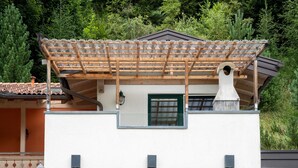 Un edificio de dos pisos con una pérgola de madera en el nivel superior, un ventanal verde y una chimenea.