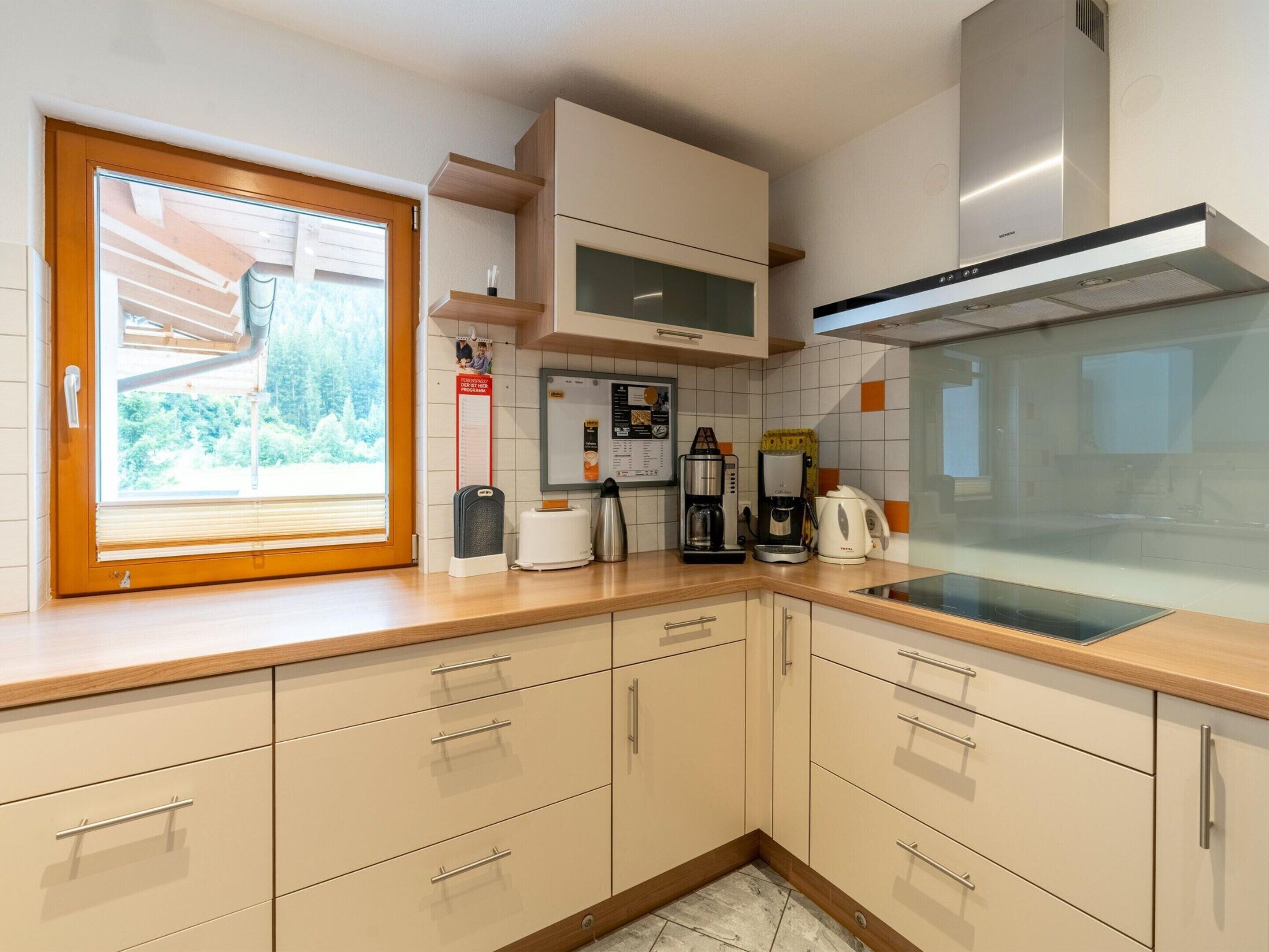 A modern kitchen with wooden cabinets, a built-in oven, a coffee maker, and a window with a view of greenery.