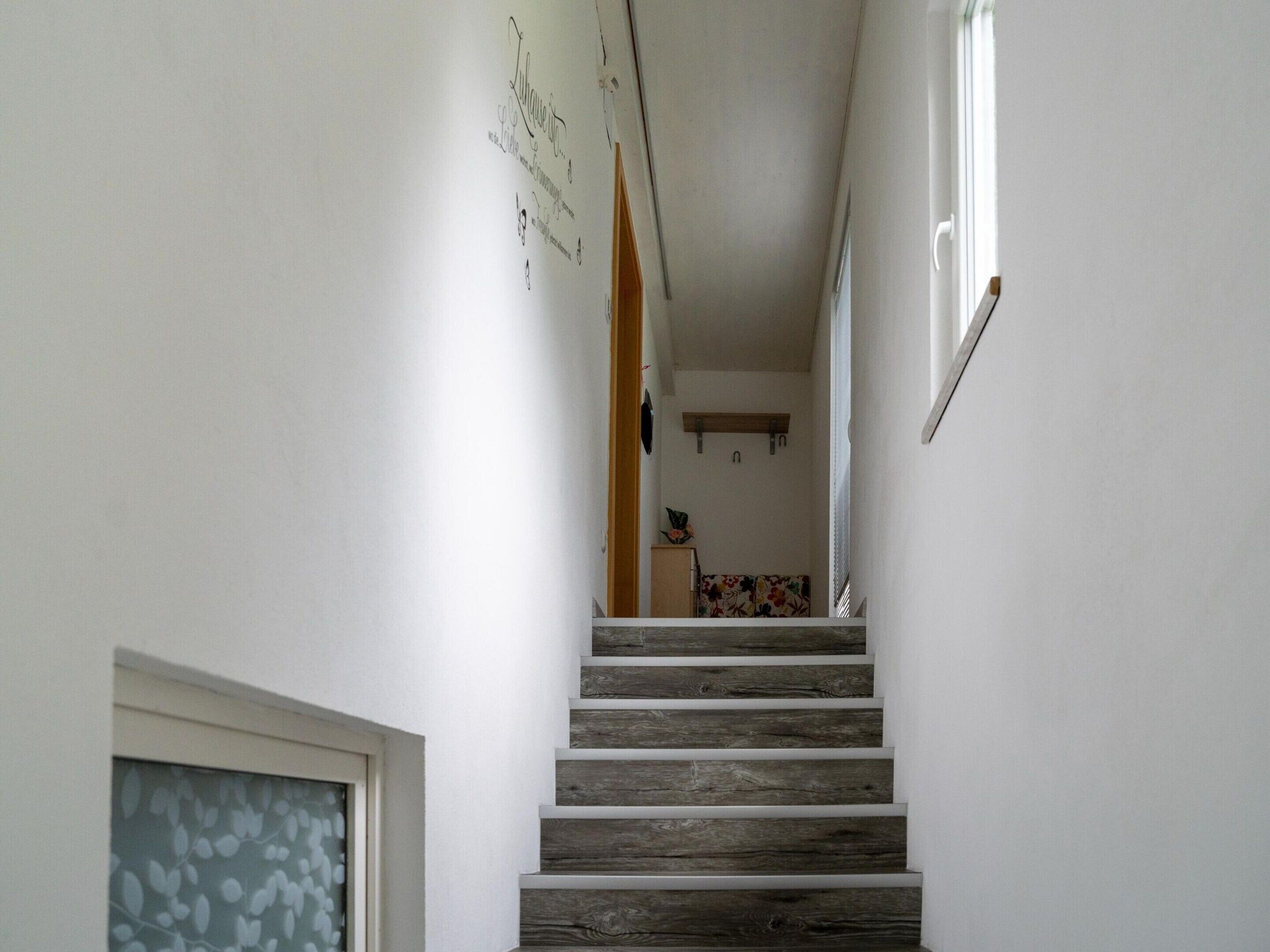 Un escalier étroit avec des marches en bois menant à une pièce dont l’un des murs est décoré d’un motif floral.