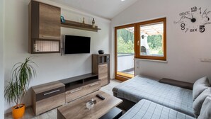 Un salón moderno con televisor de pantalla plana, muebles de madera, una planta en maceta y un amplio ventanal con vistas a zonas verdes.