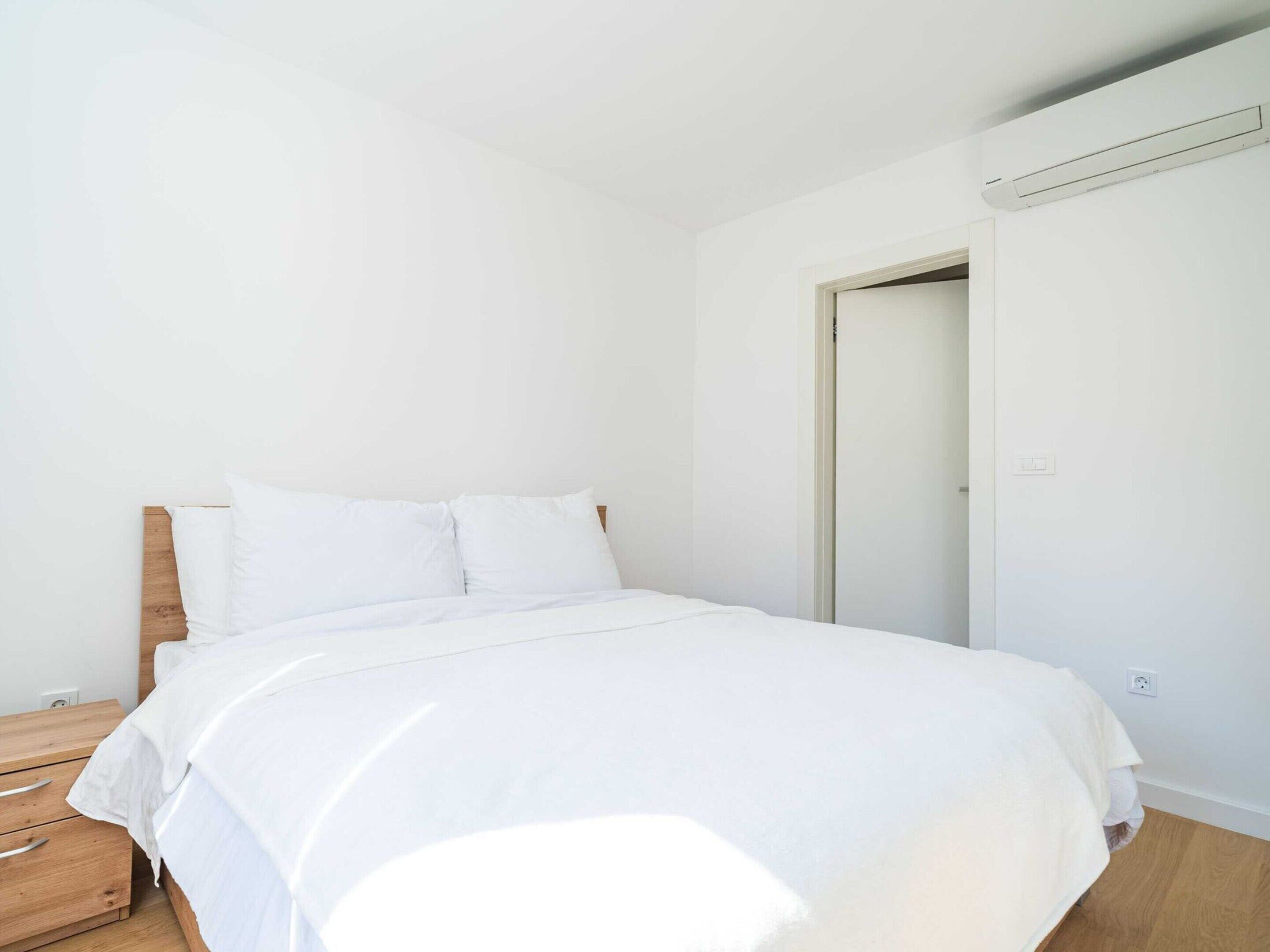 Une chambre à coucher au style minimaliste, avec un cadre de lit en bois, du linge de lit blanc et une table de chevet en bois.