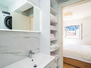 Een moderne badkamer met een ingebouwde wasmachine, een grote spiegel en een bed met uitzicht op een bergachtig landschap.