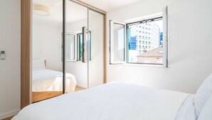 A bedroom with a large bed, a sliding door closet, and a window with a view of buildings. - Apartment Villa Claudia (Dubrovnik)