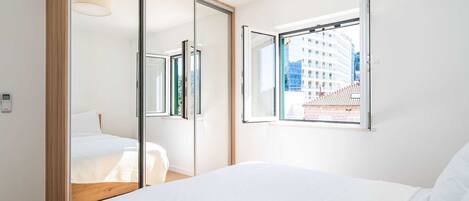 Un dormitorio con una cama grande, un armario con puerta corredera y una ventana con vista a edificios.