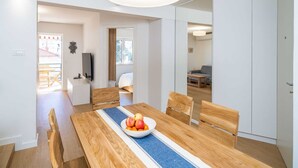 A modern dining area with a wooden table, chairs, and a bowl of fruit. There is a large white pendant light above the table. - Apartment Villa Claudia (Dubrovnik)