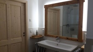 Un baño con puerta de madera, lavamanos blanco, espejo y ducha.