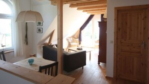 A cozy room with a wooden ceiling, a dining table with chairs, a sofa, and a large window with curtains. - Holiday Home Water View (Rankwitz)
