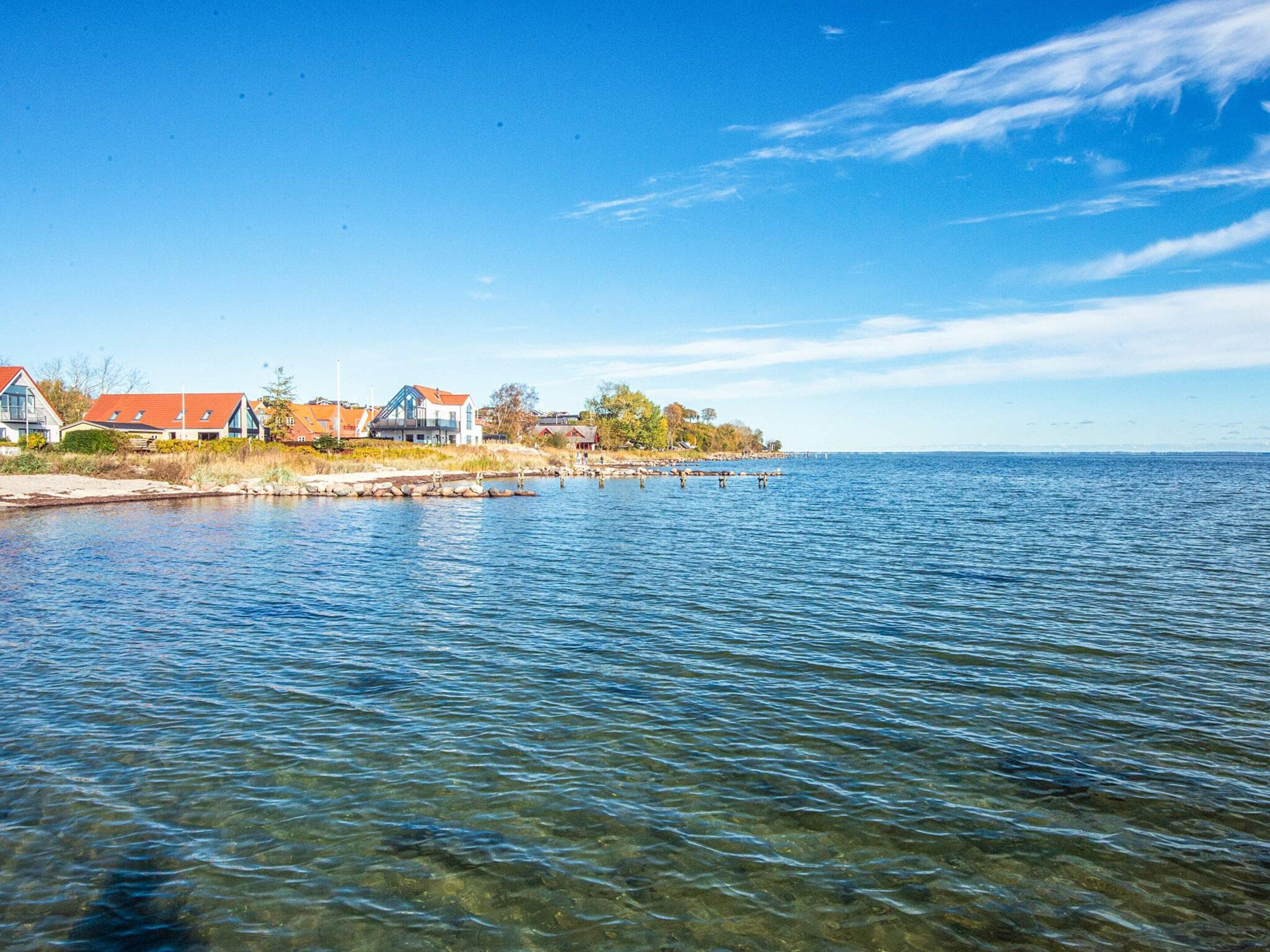 A waterfront property with a clear view of the water, a dock extending into the lake, and a row of houses with red roofs.