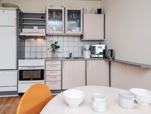 A compact kitchen with a stove, oven, and a coffee maker. There is a dining table with white cups and a chair. - 4 Person Holiday Park Home in Hejls (Hejls)