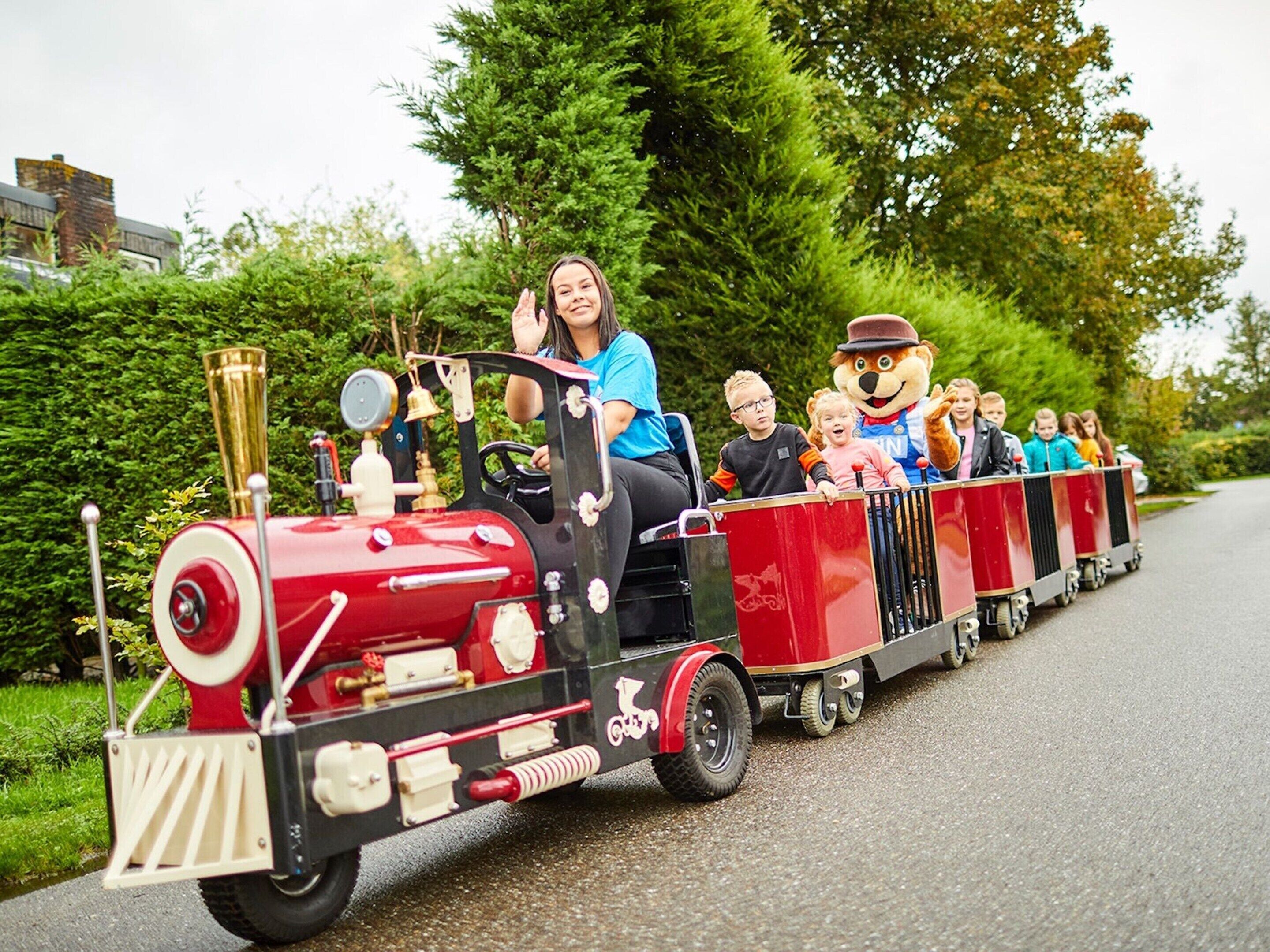 A miniature train with passengers and a mascot.