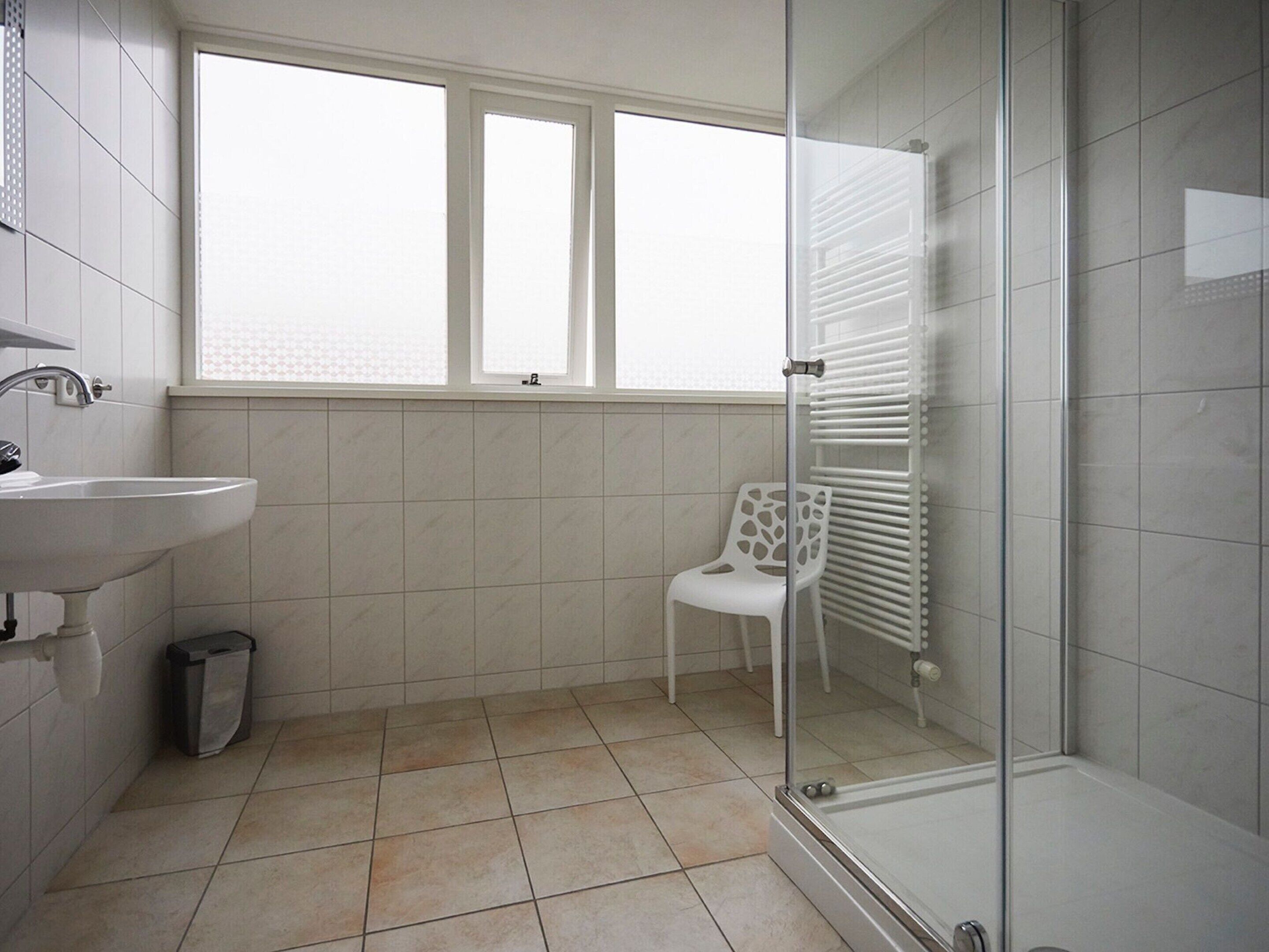 Un bagno con lavandino, una sedia, box doccia in vetro e termosifone.