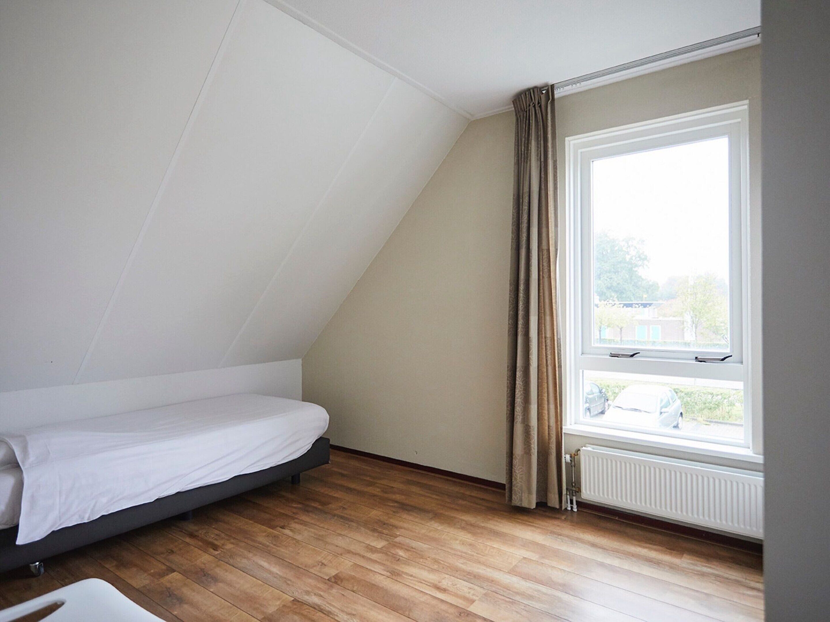 A room with a single bed, a window with curtains, and a radiator.