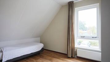 A room with a single bed, a window with curtains, and a radiator.