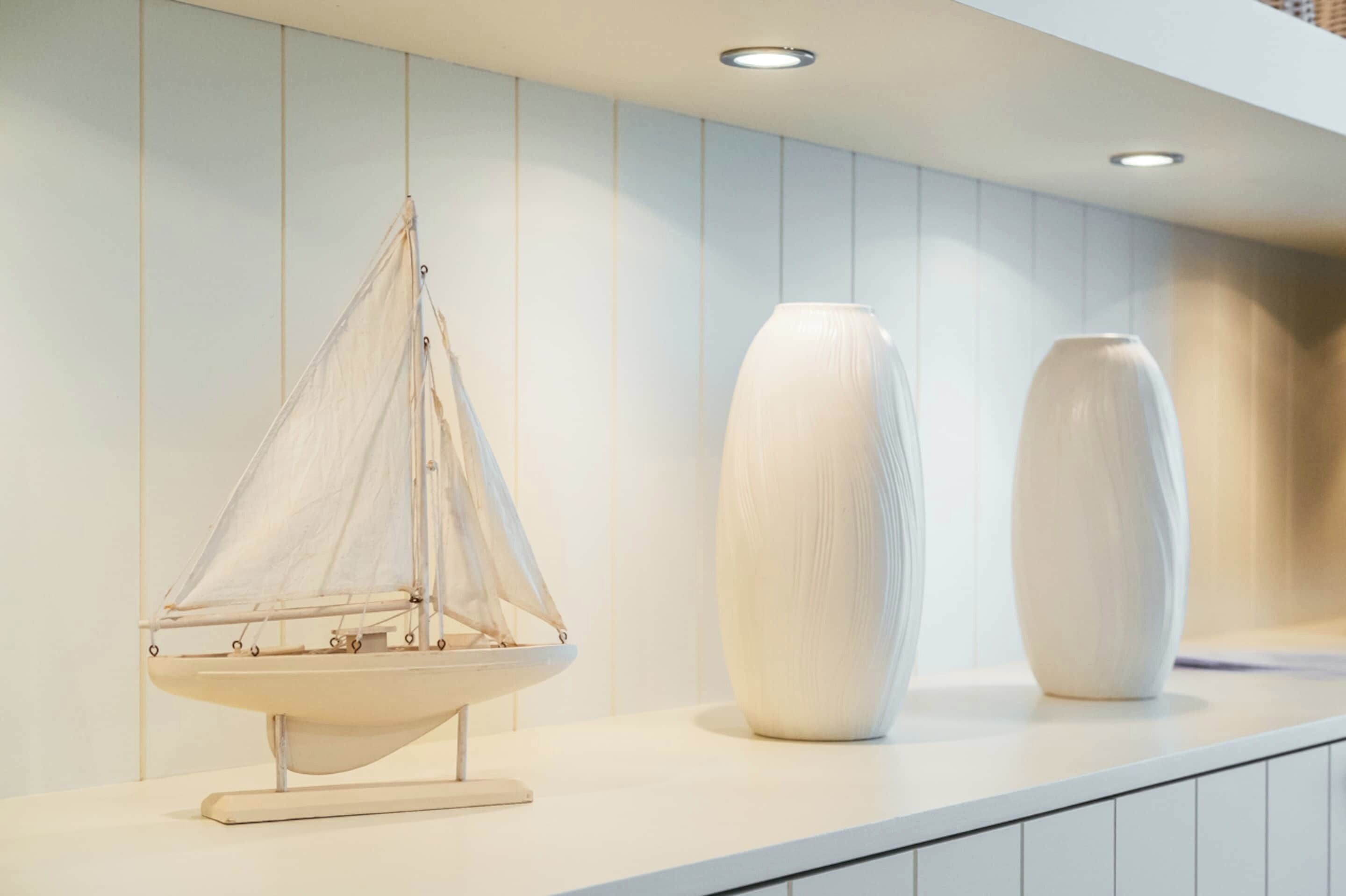A model sailboat on a white countertop, flanked by two white vases.