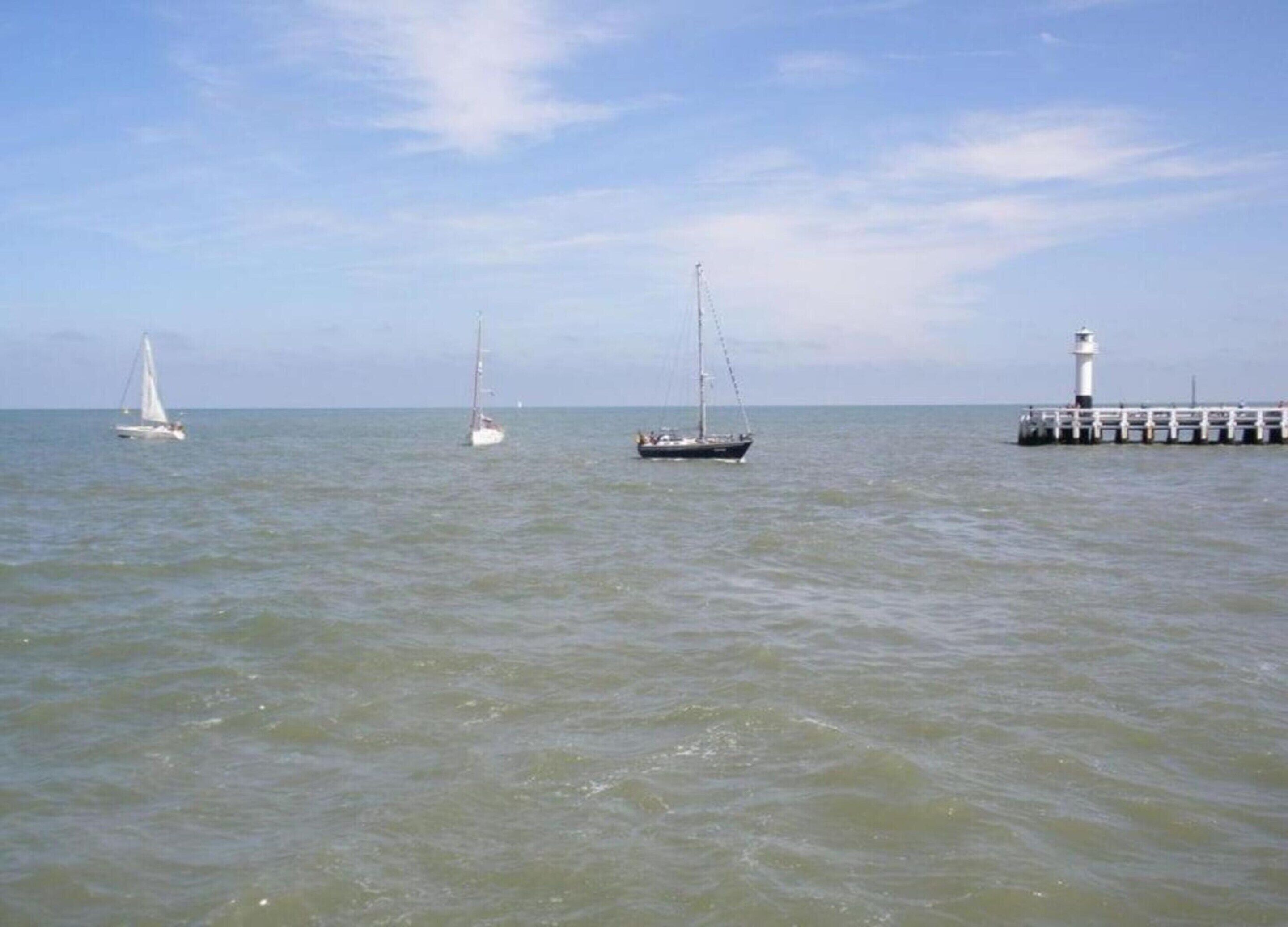 A calm sea with three sailboats and a lighthouse in the distance.