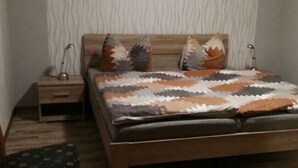 Une chambre à coucher avec un lit en bois, des coussins à motifs, une table de chevet, une chaise et un mur à texture.
