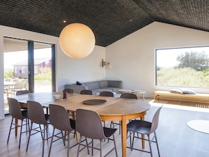Een moderne eetruimte met een grote houten tafel, grijs gestoffeerde stoelen en een hangende lamp.