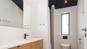 Um banheiro moderno com toucador branco, chuveiro e vaso sanitário.