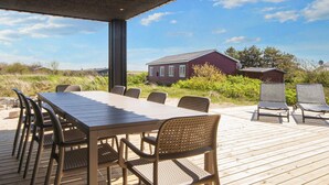 Um deck de madeira com mesa e cadeiras, com vista para uma casa vermelha e paisagem natural.