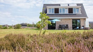 Ein zweistöckiges Haus mit Ziegeldach, einer Terrasse mit Gartenmöbeln und einem grünen Rasen im Vordergrund.