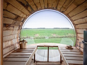 A circular wooden structure with a bench and a table, a bucket, and a plate with food items. - Stylish Texel Escape With Spa (Den Burg)