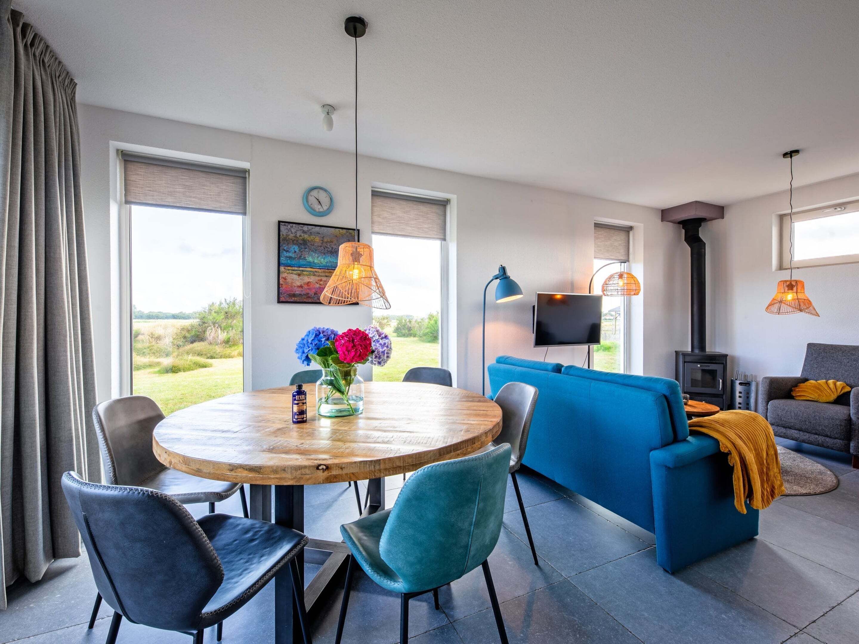 Sala de estar moderna com mesa de madeira redonda, sofá azul e televisão.