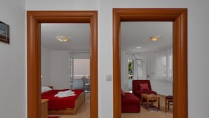 A hotel room with a bed, a red sofa, a small table, and a chair. There is a window with curtains and a view of the outside. - Apartments Villa Juric - One-bedroom Apartment (Baska Voda)
