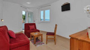 A living room with a red sofa, a wooden chair, a small table, and a TV on the wall. - Apartments Villa Juric - One-bedroom Apartment (Baska Voda)