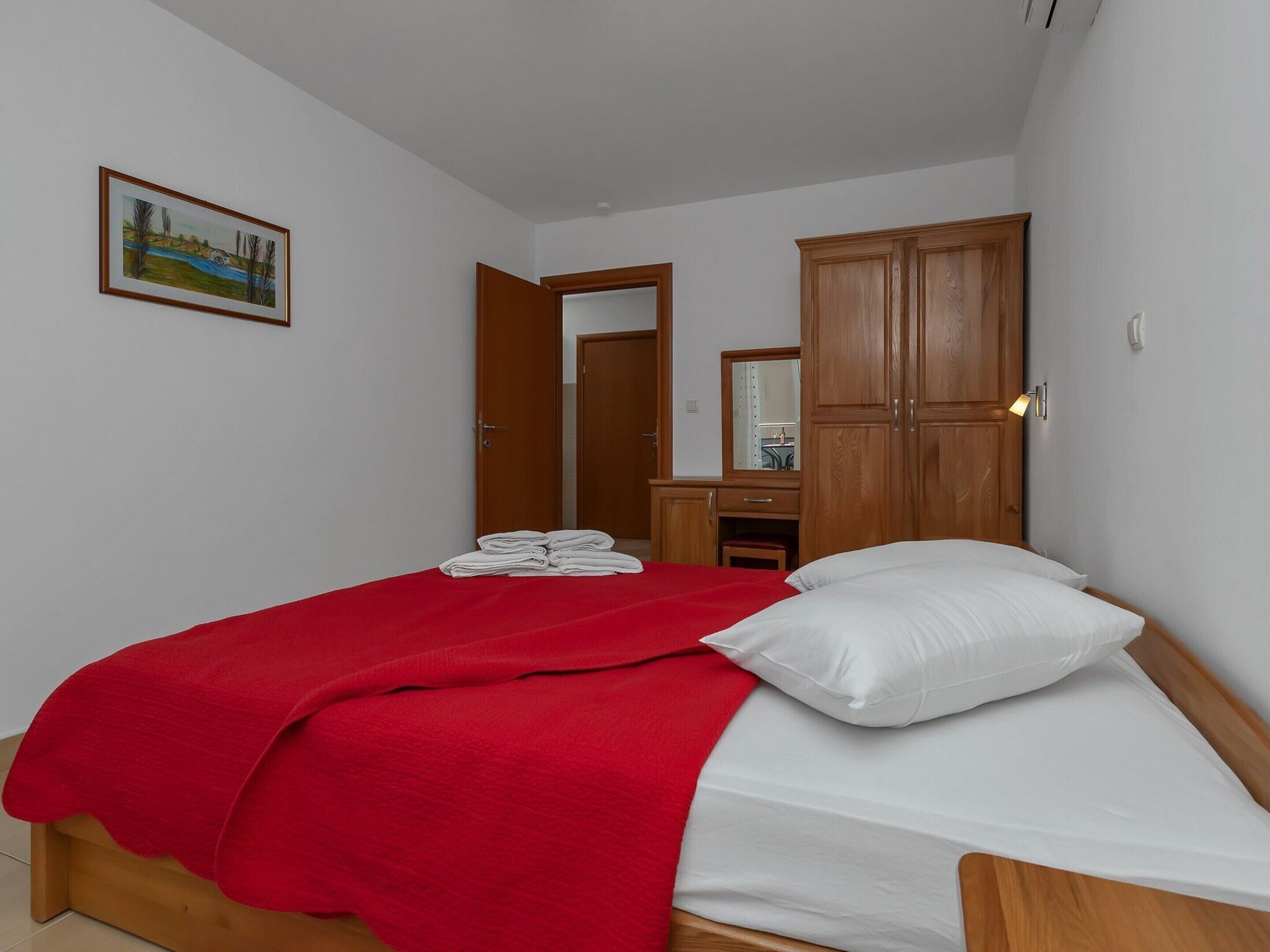 Quarto com uma cama, um guarda-roupa de madeira, um espelho e um quadro na parede.