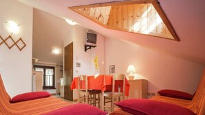 Een knus ingerichte kamer met twee bedden, een houten plafond, een bureau met stoel en een televisie aan de muur.