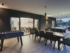 A modern indoor space with a pool table, foosball table, and a dining area with chairs and a table.