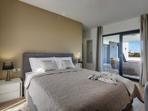 A modern hotel room with a large bed, a bedside table with a lamp, and a view of the outdoor balcony.