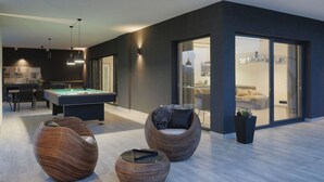 Een moderne woonkamer met een pooltafel, twee loungestoelen en een eethoek met een tafel en stoelen.